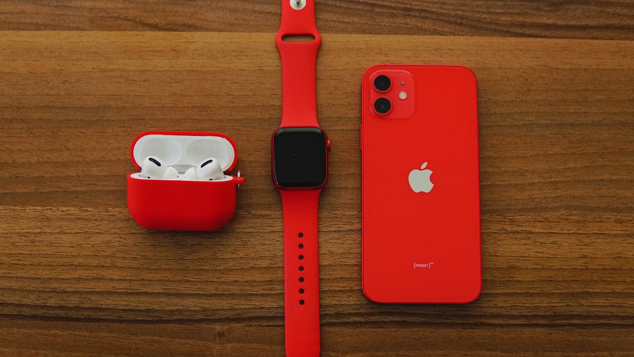 hero-img-01 Top view flat lay of red apple watch, iPhone, and AirPods on wooden table.